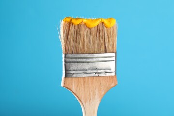 Brush with yellow paint on light blue background, closeup