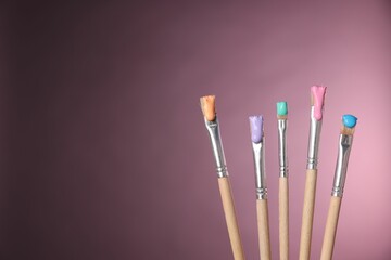 Many brushes with color paints on pink background, closeup. Space for text
