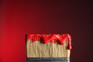 Brush with paint on red background, closeup. Space for text