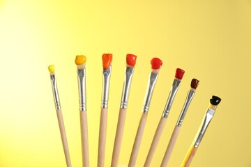 Many brushes with color paints on yellow background, closeup