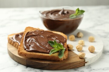 Tasty chocolate spread with mint and hazelnuts on white marble table, closeup