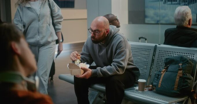 Crowded International Airport Terminal: Man Eating Burger, Waiting for Delayed Airplane Flight, Going on Trip. Diverse People, Passengers Sitting in Boarding Lounge of Airline Hub. Tourism and Travel.
