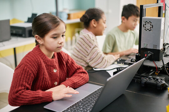 Diverse group of students engaged in coding and programming activities at technology class, with focus on female student using laptop and other students in background working on devices