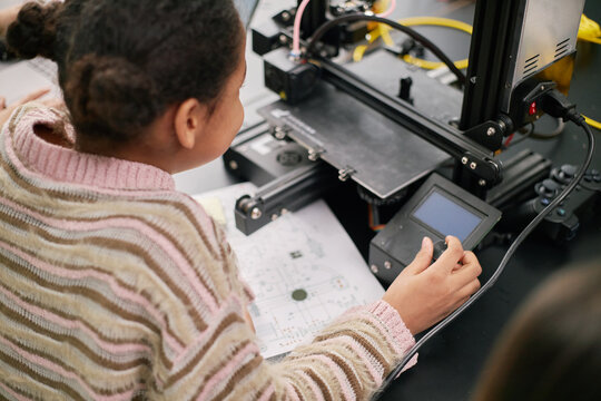 Student working on technology project in classroom setting with 3D printer and various equipment visible. Engaging in hands-on learning experience - Powered by Adobe