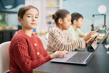 Group of children immersed in using laptops and tablets, working together in a colorful classroom environment. Laptops and tablets are prominently featured on tables