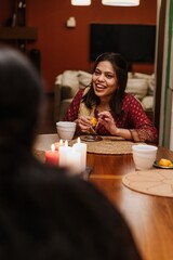 A woman sits at a table and smiles while holding food and looking at her female friend sitting across from her