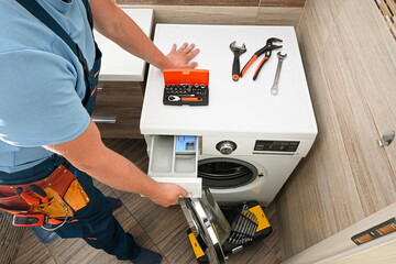 Repairman opening the detergent drawer of a washing machine during maintenance, with tools on top...