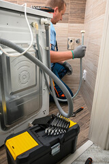 Plumber working on installing a washing machine drain hose in a bathroom, using tools and expertise to ensure proper function