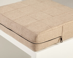 Beige fabric cushion resting on white surface with zipper detail