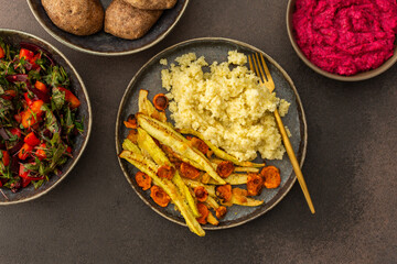 This nutritious meal features millet with baked zucchini and carrots, complemented by a vibrant salad of fresh seasonal vegetables and herbs, alongside chickpea buns and creamy beetroot hummus