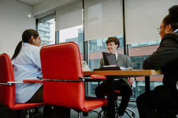 Fototapeta premium Male intern and two female employees sitting at a table and laughing, in the office
