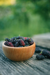 Fresh ripe mulberries in a wooden bowl on rustic wooden table. Juicy berries with deep red and purple tones, perfect for summer desserts or healthy snacks