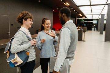 Male and female employees and male intern standing and talking while laughing, in a hall