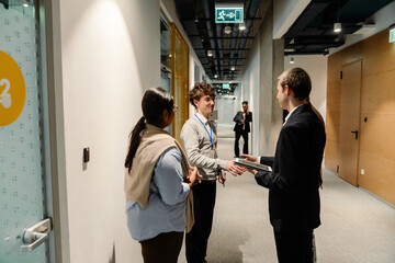 A male intern stands and is about to shake hands with one of the three employees standing next to...