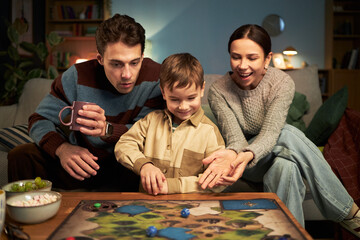 Fototapeta premium Happy family playing board game together with little son at table in the room