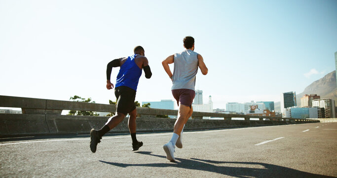 Men, back and running with road in city for workout, exercise or outdoor cardio training. Active, male people or runners with fitness on street for sport, marathon or sprint together in an urban town