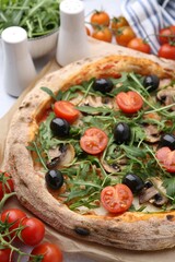 Tasty pizza with cherry tomatoes, black olives, mushrooms and arugula on table, closeup