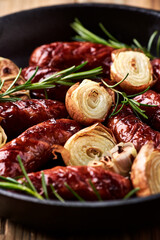 Fried sausages with fresh rosemary in cast-iron pan. Close up. 	