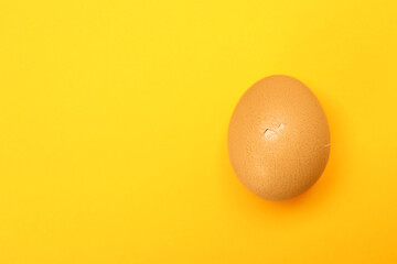 One egg with cracked shell on orange background, top view. Space for text