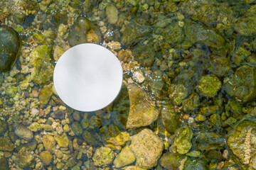 Product podium placed on clear water with pebbles and stones surrounding it during a sunny day