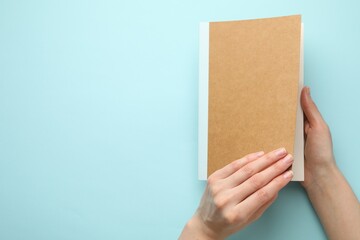 Woman with copybook on light blue background, top view. Space for text