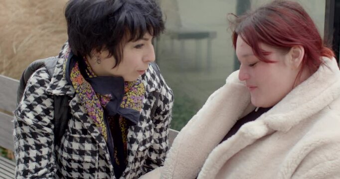Two women are sitting on a park city bench, engaging in a heartfelt and meaningful dialogue with each other