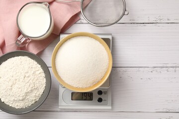 Digital kitchen scale with bowl of sugar and other products on white wooden table, flat lay. Space for text