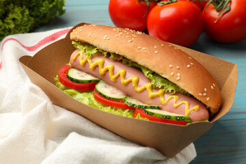 Tasty hot dog with vegetables on blue wooden table, closeup