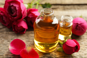 Open perfume bottles with aromatic essential oils and roses on wooden table, closeup
