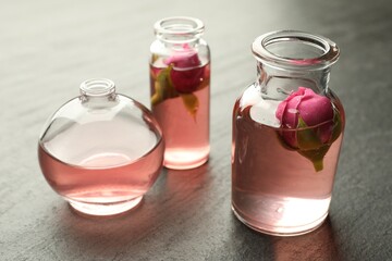 Open perfume bottles with aromatic essential oils and roses on grey textured table, closeup