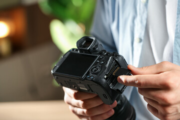 Man inserting SD memory card into photo camera indoors, closeup. Space for text