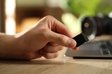 Man with SD memory card at wooden table indoors, closeup