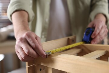 Man measuring wooden stool with tape indoors, closeup
