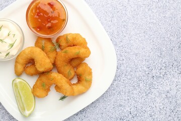 Tasty tempura shrimps, lime and sauces on grey textured table, top view. Space for text