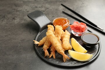 Tasty tempura shrimps, lemon, ginger and sauces on grey textured table, closeup. Space for text