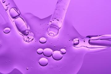 Transparent serum and several cosmetic pipettes on a lilac background. The texture.