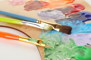 Wooden palette with paints and brushes on white background, closeup