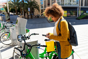 Young woman renting a bicycle using her smartphone in the city