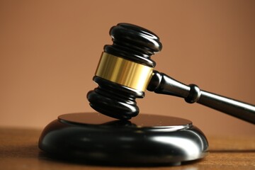 Judge's gavel and sound block on wooden table against pale brown background, closeup