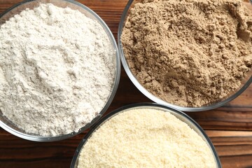 Different types of flour in bowls on wooden table, top view