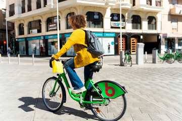 Fototapeta premium Young latin american woman riding a shared bicycle in the city