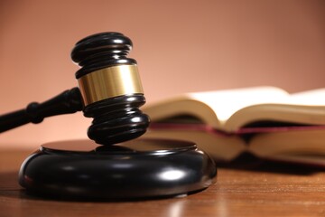 Judge's gavel, sound block and books on wooden table against pale brown background, closeup