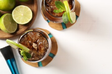 Tasty Cuba Libre cocktail in glasses, limes and muddler on white table, flat lay. Space for text