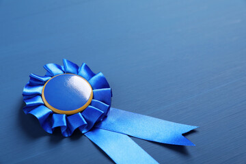 Award ribbon on blue wooden table, closeup. Space for text