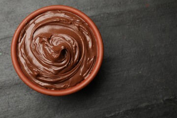 Tasty chocolate spread in bowl on black table, top view. Space for text
