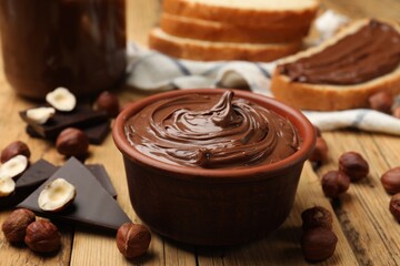 Tasty hazelnut spread, chocolate pieces and nuts on wooden table, closeup