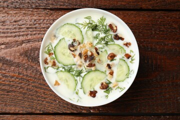 Tasty cucumber soup with dill and nuts in bowl on wooden table, top view