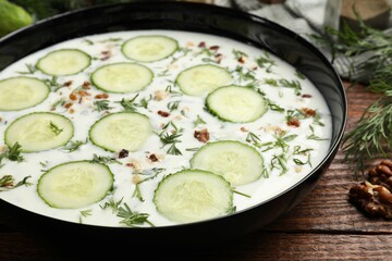 Fresh tasty cucumber soup and ingredients on wooden table, closeup