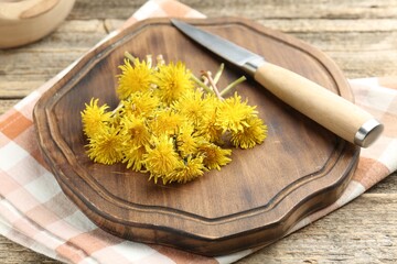 Dandelion flowers, knife and cutting board on wooden table, closeup