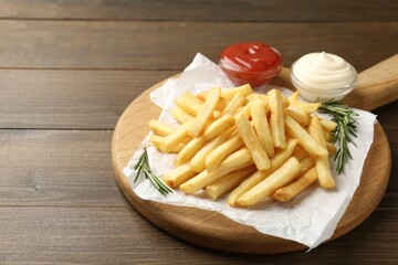 Tasty french fries with sauces and rosemary on wooden table, closeup. Space for text